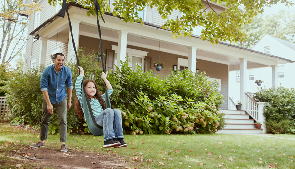 Father pushing daughter on swing in their house front yard